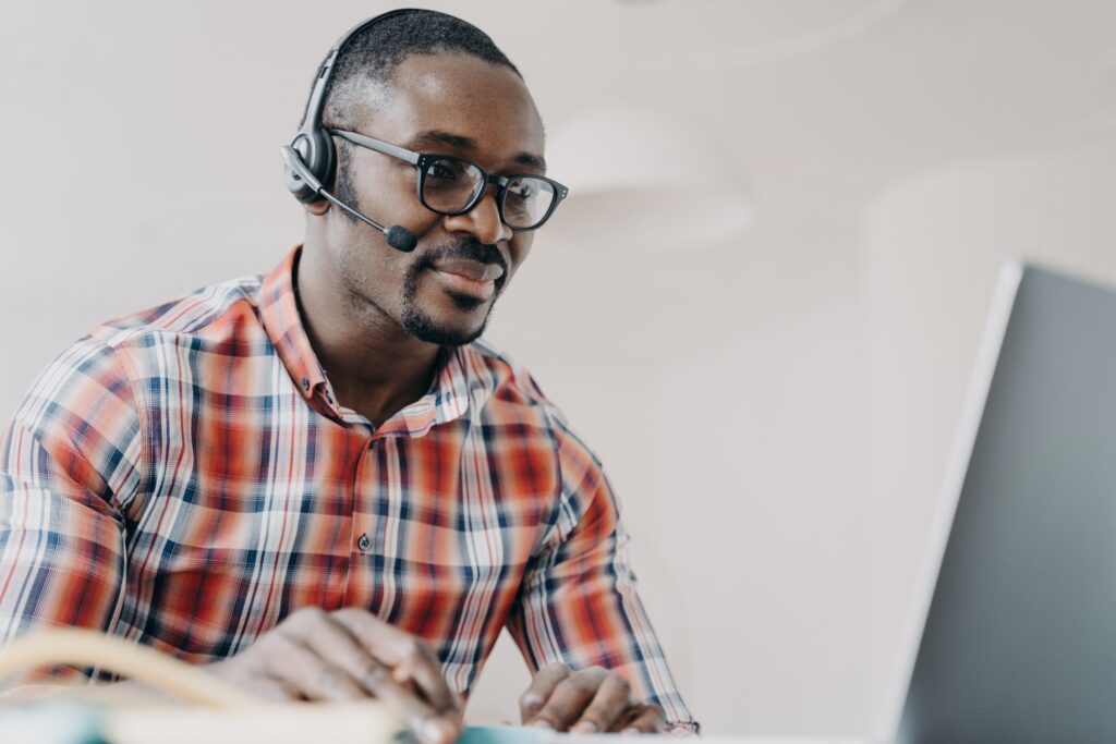 African american male support services worker wearing headset working at laptop. Remote job