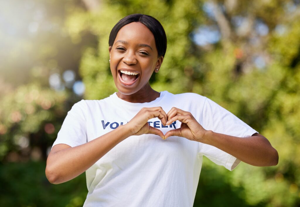 Heart, hands and portrait of volunteer woman with sign for care, support and charity outdoor in nat